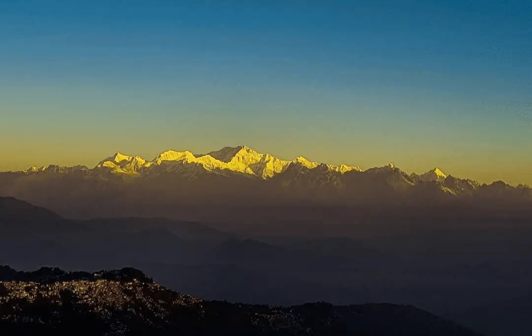 Majestic snow-capped mountains against a vibrant blue and yellow sky, with silhouetted hills in the foreground